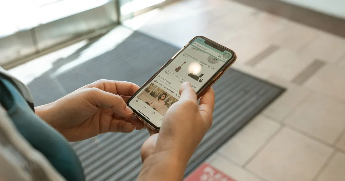 Người dùng cầm điện thoại xem một trang web bán hàng trên bàn gỗ