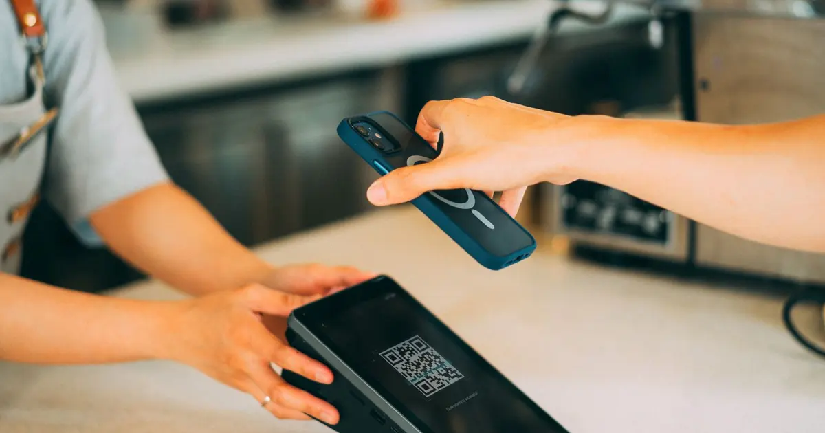 Bàn tay đưa điện thoại quét mã QR trên máy tại quầy quán